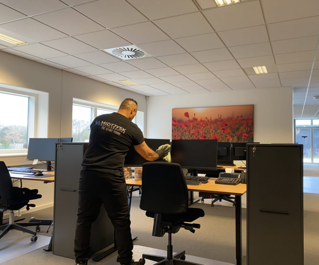 Rengøringsassistent pudser pc skærm i et kontor